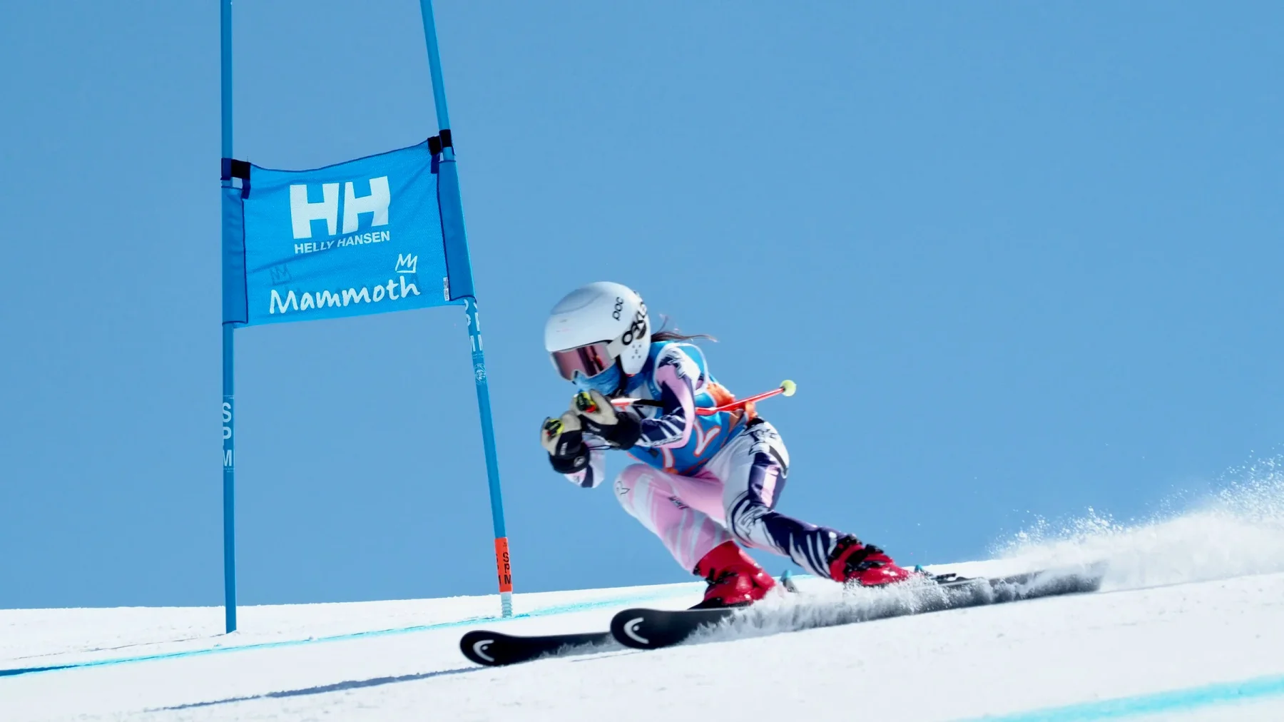 Skier in a low turn passing a blue race gate, with snow spraying from the skis